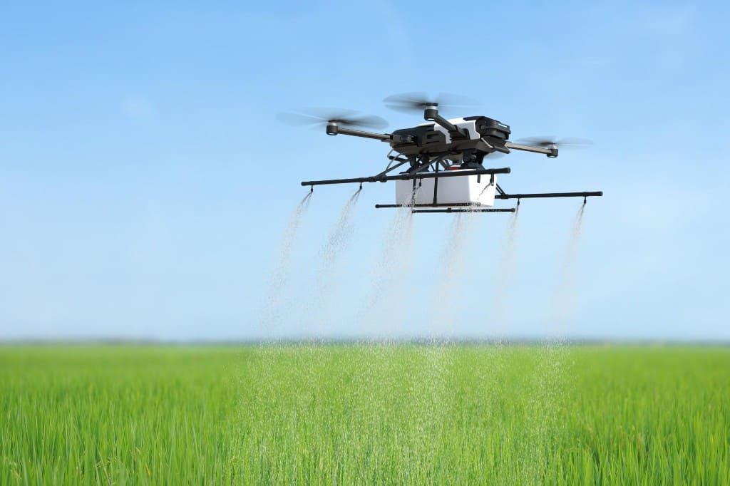 Agricultural drone spraying fertilizer over a lush green commercial field under a clear sky